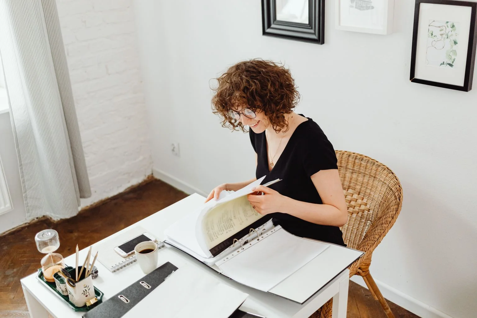Une jeune femme consulte et classe des documents dans un classeur, à une table chez elle.